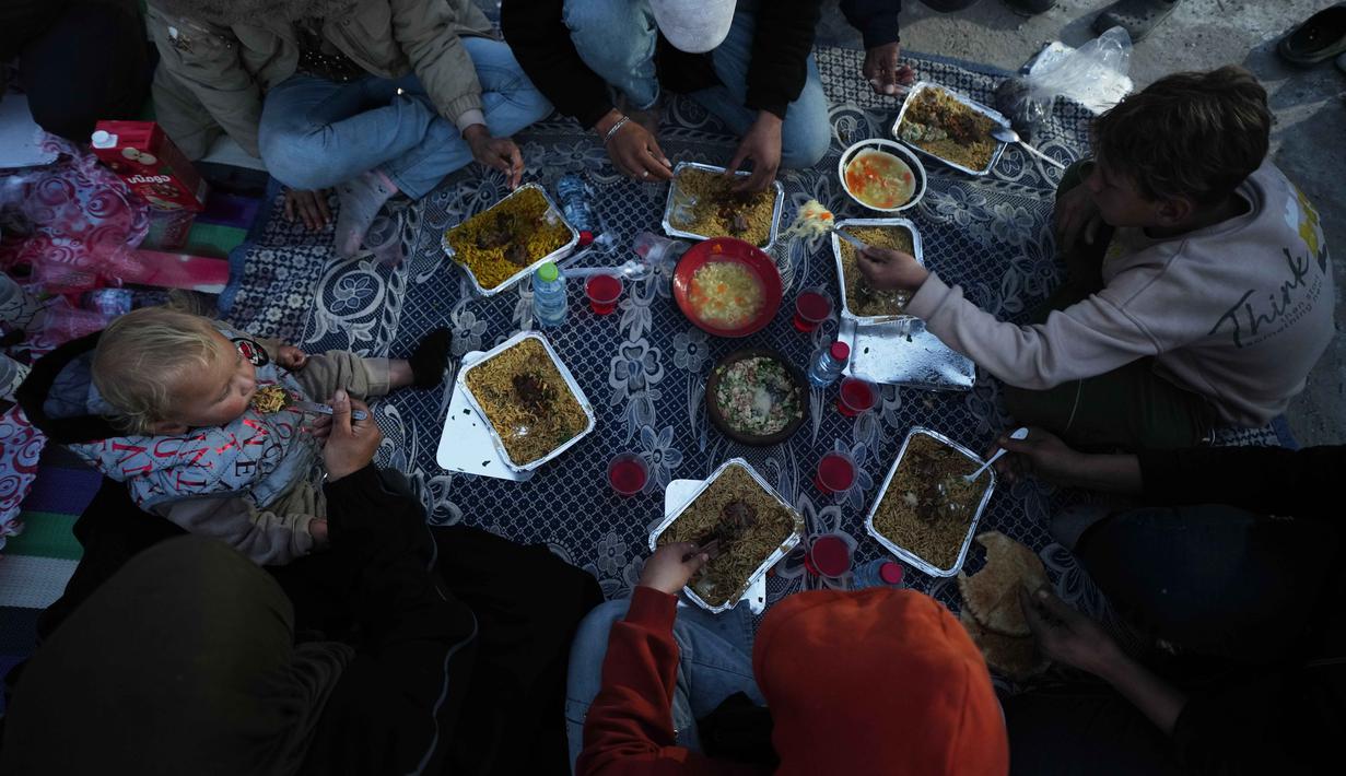 Di beberapa titik di kota Gaza, warga berkumpul bersama keluarga menggelar makanan sederhana untuk berbuka puasa bersama, seperti roti, kurma, dan air minum di lokasi yang dulunya merupakan rumah atau bangunan tempat mereka beraktivitas. Tampak dalam foto, anggota keluarga Al-Najar berbuka puasa selama bulan suci Ramadan di tengah reruntuhan bangunan yang hancur di Kota Gaza, Jumat 13 Maret 2026. (AP Photo/Jehad Alshrafi)