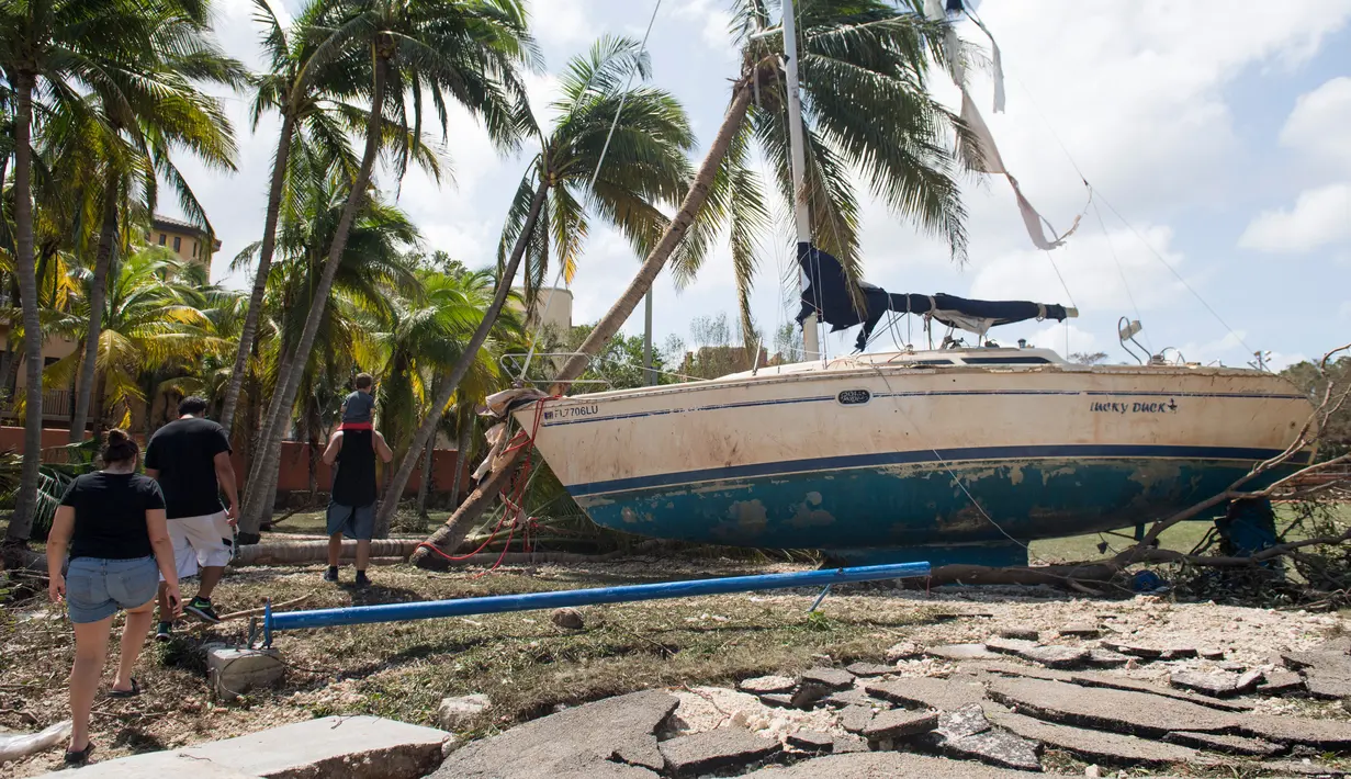 Sejumlah orang berjalan menghampiri sebuah kapal yang terhempas ke daratan akibat tersapu badai Irma di Coconut Grove, Florida, Senin (11/9).Badai Irma menghantam negara bagian Florida dengan kecepatan angin mencapai 200 km/jam. (SAUL LOEB/AFP)