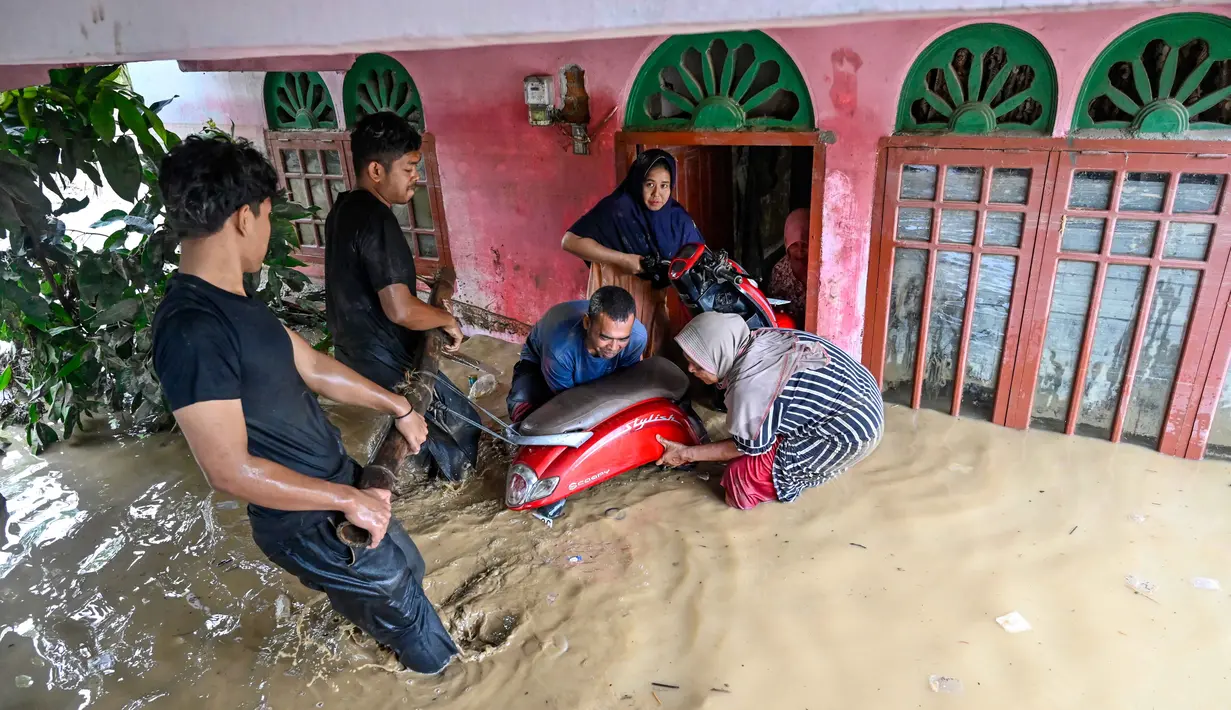 Wilayah-wilayah terparah yang tertimbun material sisa banjir adalah desa-desa di Kecamatan Meureudu, Meurah Dua dan Ulim. Tampak dalam foto, warga memindahkan sepeda motor di tengah banjir bandang di Meureudu, Kabupaten Pidie Jaya, Provinsi Aceh, Jumat 28 November 2025. (CHAIDEER MAHYUDDIN/AFP)