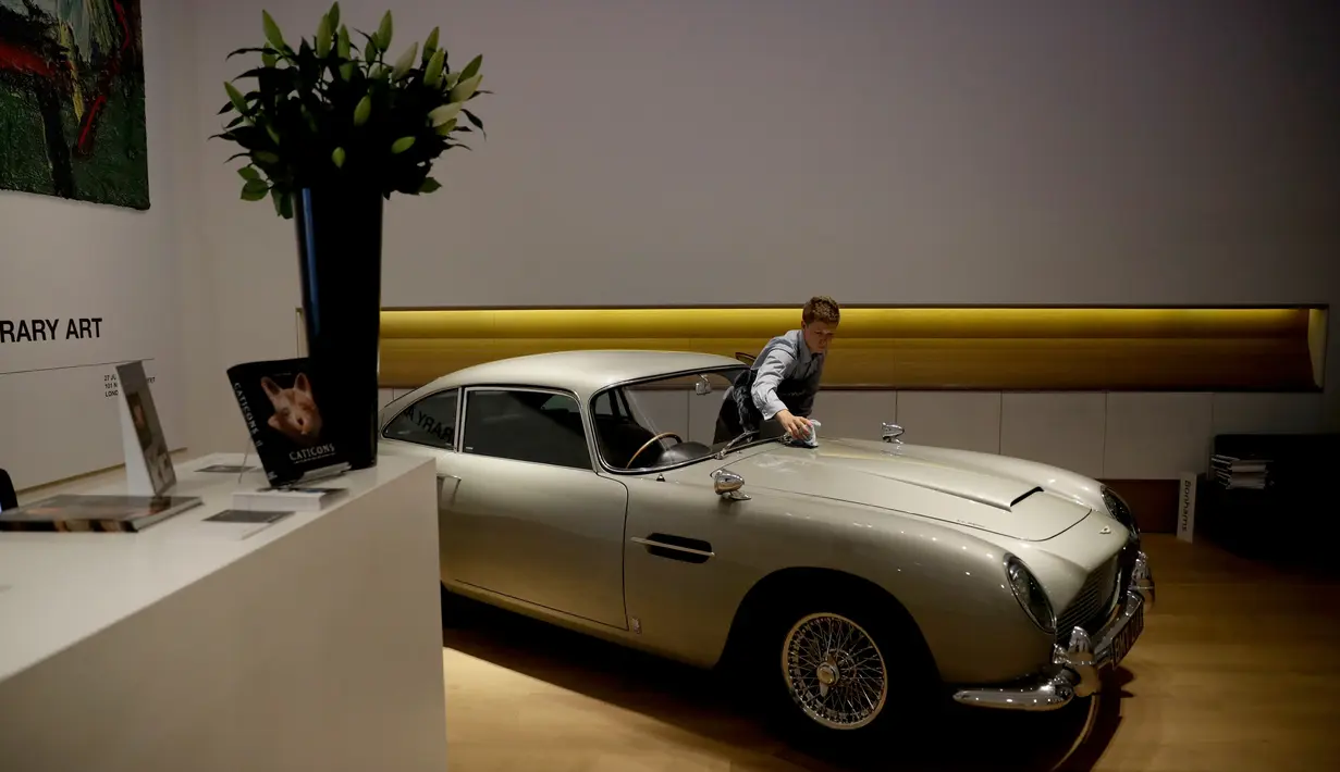 Seorang staf berpose dengan Aston Martin DB5 yang digunakan dalam film James Bond GoldenEye tahun 1995 rumah lelang Bonham, London, Selasa (19/6). Diproduksi mulai 1963 sampai 1965, Aston Martin DB5 bukanlah mobil biasa. (AP/Matt Dunham)