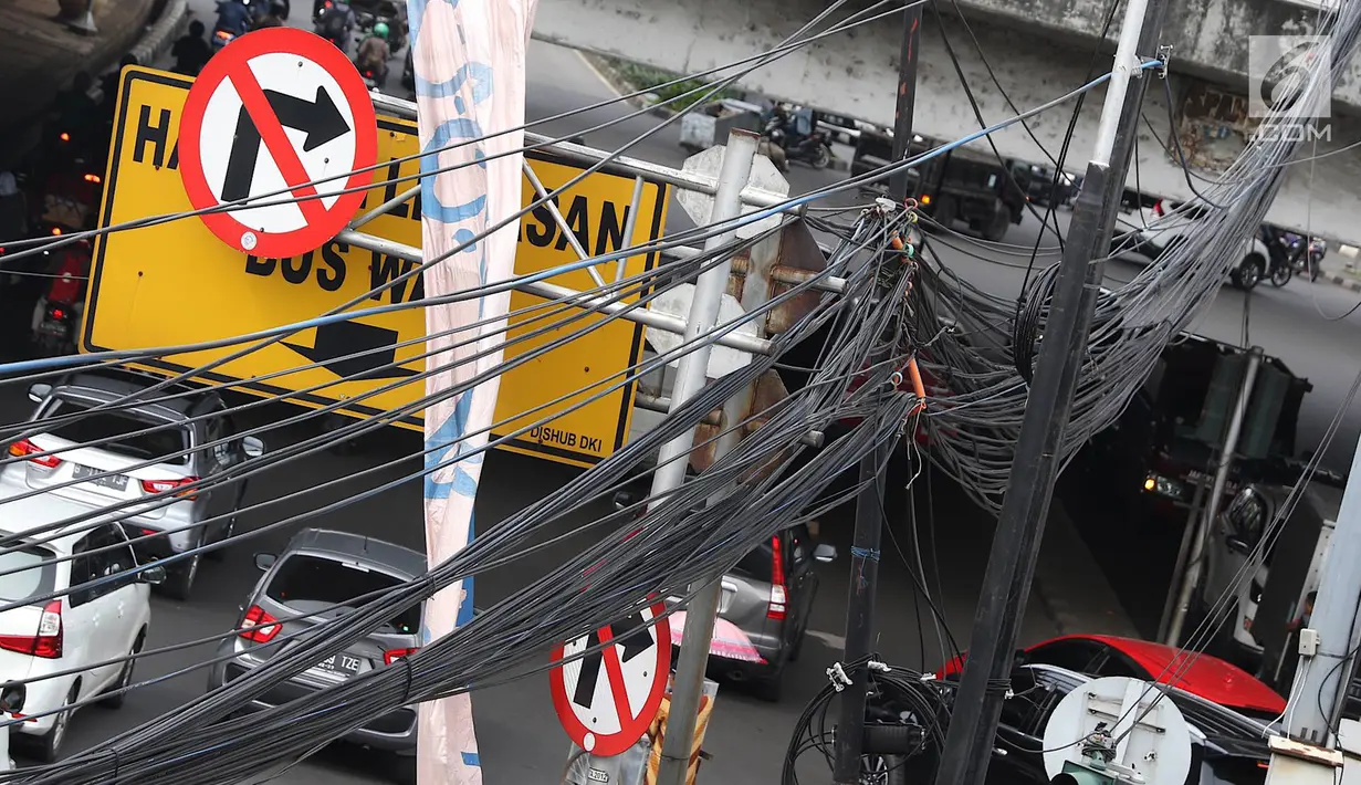 Instalasi kabel semrawut menjuntai di Jalan Dewi Sartika, Jakarta Timur, Sabtu (19/1). Selain mengganggu keindahan kota, kondisi tersebut juga berbahaya karena dapat memicu hubungan pendek arus listrik. (Liputan6.com/Immanuel Antonius)