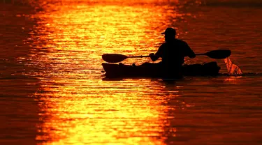 Seorang pria melintasi pantulan matahari terbenam saat berperahu di Shawnee Mission Lake, Shawnee, Kansas, Amerika Serikat, Jumat (9/10/2020). Matahari terbenam terus lebih cerah dari biasanya karena asap dari kebakaran hutan barat terus melayang di seluruh negeri. (AP Photo/Charlie Riedel)