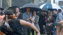 Pangeran Harry dan Meghan Markle berlindung di bawah payung menyaksikan tarian aborigin saat piknik di Victoria Park, Dubbo, Australia, Rabu (17/10). Keduanya diagendakan tur ke Australia dan Pasifik Selatan selama 16 hari. (Ian Vogler/Pool via AP)