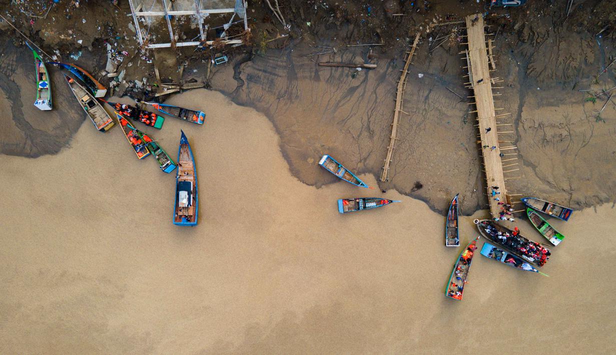 Inisiatif ini muncul dari para nelayan setempat yang secara mandiri menyediakan layanan penyeberangan untuk membantu warga dari kedua sisi sungai. Tampak foto menunjukkan para penumpang menaiki perahu untuk menyeberangi Sungai Peusangan di Kuta Blang, Kabupaten Bireuen, Provinsi Aceh, Selasa 9 Desember 2025. (CHAIDEER MAHYUDDIN/AFP)