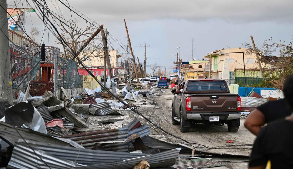 Sebuah mobil melaju melewati lingkungan yang hancur akibat Badai Melissa di Black River, Jamaika, pada 29 Oktober 2025. Badai Melissa menyebabkan kerusakan parah pada infrastruktur jalan raya, jaringan komunikasi, dan jaringan listrik, membuat sebagian besar wilayah mengalami pemadaman listrik. (Ricardo MAKYN/AFP)