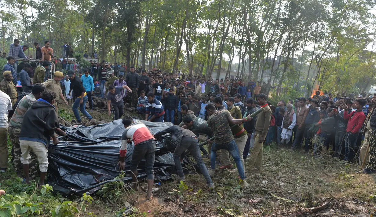 Polisi dan pekerja kehutanan bersama penduduk desa menutupi tubuh gajah betina dengan  plastik, yang sedang hamil, setelah kereta penumpang yang melaju menabrak dua gajah yang melintasi rel di desa Batasi dekat perbatasan India-Nepal, sekitar 37 km dari Siliguri (11/12/2019). (AFP/Diptendu Dutta)