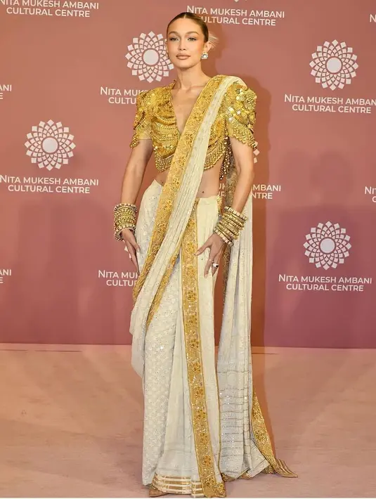 Gigi Hadid mengenakan blus permata emas dan saree Chikankari putih. Melansir NDTV, kain sari yang ia kenakan dihiasi dengan pinggiran patti emas dan menampilkan celah setinggi paha di sampingnya. Penampilannya semakin menawan dengan sanggul ramping, gelang emas bertumpuk, dan sepatu hak tinggi. (Liputan6.com/IG/@gigihadid)