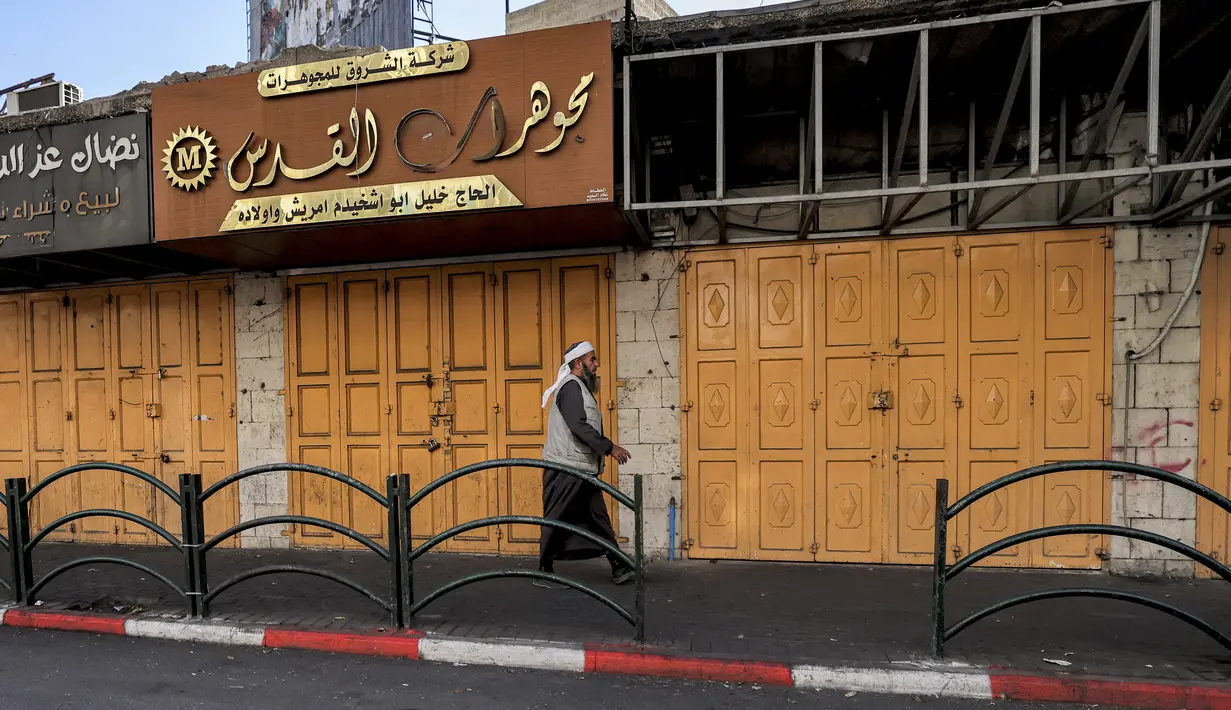 Seorang pria berjalan melewati toko-toko yang tutup di sepanjang jalan di kota Hebron di Tepi Barat yang diduduki saat terjadi pemogokan umum yang diserukan sebagai tanggapan atas serangan ke kompleks rumah sakit di Gaza, Rabu (18/10/2023). (HAZEM BADER / AFP)