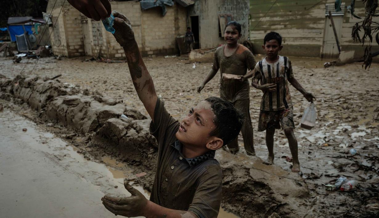 Sebagai informasi, hingga Selasa 16 Desember 2025, Kabupaten Aceh Tamiang masih berada dalam fase pemulihan setelah dihantam banjir bandang pada akhir November 2025 lalu. Tampak dalam foto, seorang anak menerima uang kertas dari seseorang di truk distribusi di Babo, Aceh Tamiang, pada Senin 15 Desember 2025. (Yasuyoshi CHIBA/AFP)