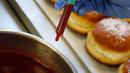 Seorang pekerja menyiapkan jarum suntik yang penuh dengan jeli raspberry saat membuat berliner (donat Jerman) di toko roti Kreyenbuhl di Muri, Swiss, 5 Februari 2021. Pembeli dapat menyuntikkan sendiri "vaksin" ke dalam donut dengan pilihan rasa raspberry atau Bailey-liqueur. (STEFAN WERMUTH/AFP)