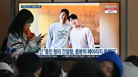 Seorang wanita berjalan melewati layar televisi yang menyajikan tayangan foto pemain Timnas Korea Selatan, Son Heung-min (kiri), dan Lee Kang-in (kanan), di Seoul, Rabu (21/2/20240. (Jung Yeon-je / AFP)