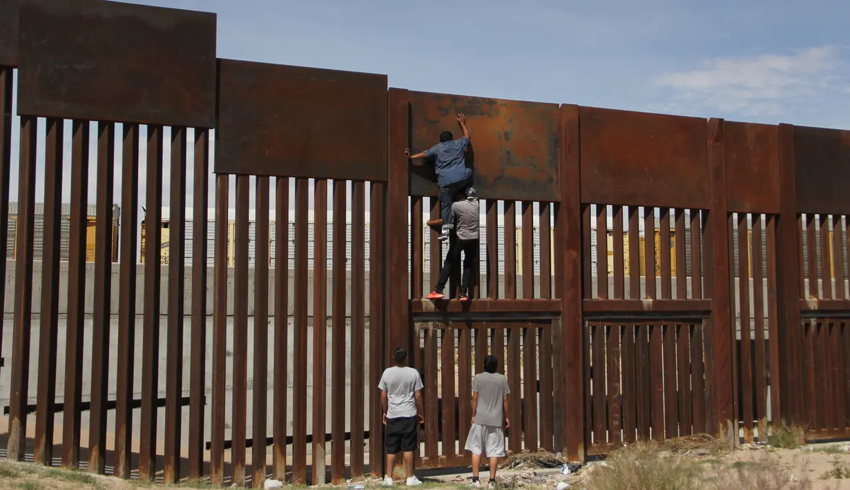 Sejumlah pemuda Meksiko berusaha memanjat tembok besi perbatasan antara Meksiko dan Amerika Serikat di negara bagian Chihuahua, Meksiko (6/4). Mereka menyeberang secara ilegal ke Sunland Park dari Ciudad Juarez. (AFP/Herika Matinez)