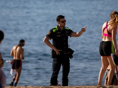 Petugas polisi meminta orang-orang untuk tidak duduk sambil berpatroli di pantai di Barcelona, Spanyol, Rabu, (20/5/2020). Barcelona mengizinkan orang untuk berjalan di pantai untuk pertama kalinya sejak dimulainya penguncian virus coronavirus lebih dari dua bulan lalu. (AP Photo/Emilio Morenatti)