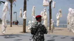 Seorang petugas keamanan berjaga dekat puluhan gaun pengantin yang digantung di tepi pantai Beirut, Sabtu (22/4). Gaun yang digantung di tepi pantai itu sebagai bentuk protes Undang-Undang Pemerkosaan di Lebanon oleh sekelompok aktivis. (PATRICK BAZ/AFP)