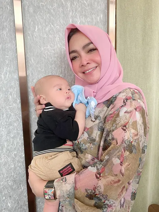 Melihat kebahagiaan Rieta Amalia, ibunda dari Nagita Slavina saat menggendong cucunya Rayyanza, putra kedua dari pasangan Raffi Ahmad dan Nagita Slavina. Di sini, Rieta tampil mengenakan kemeja bermotif bunga bernuansa merah muda yang dipadu dengan hijab polos yang senada. Foto: Instagram.