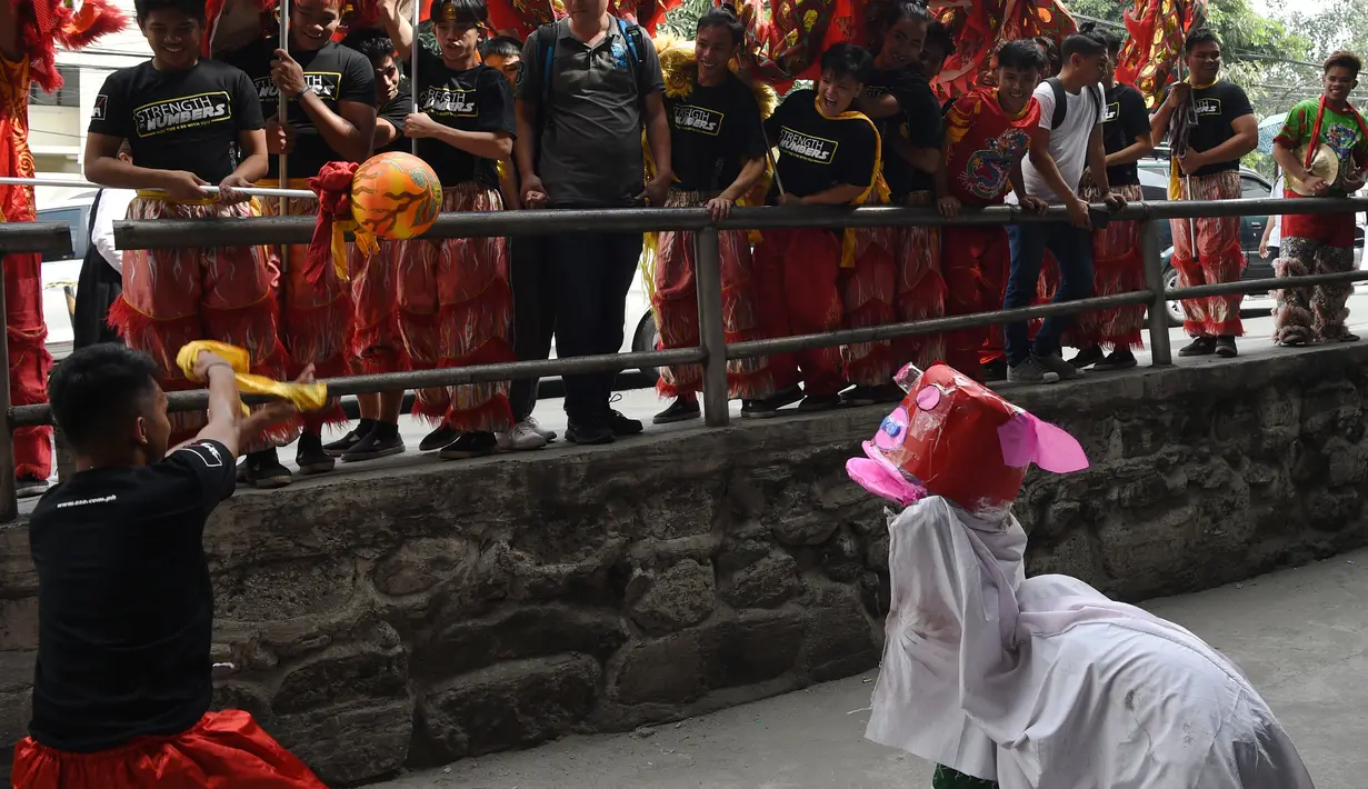 Anggota kelompok barongsai melihat aksi anak-anak melakukan tarian singa di distrik Chinatown, Manila (4/2). Anak-anak jalanan ini tampil lucu dengan alat seadanya seperti ember dan kerdus untuk menyambut Tahun Baru Imlek. (AFP Photo/Ted Aljibe)