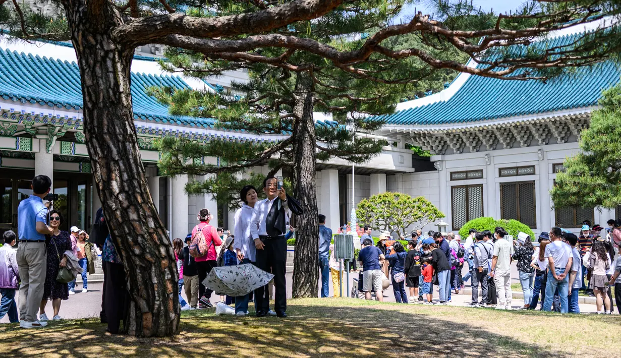 Sepasang suami istri (tengah) berswafoto saat pengunjung lain mengantre untuk berfoto di depan Blue House (belakang) sehari setelah kompleks tersebut dibuka untuk umum sesuai janji kampanye Presiden Korea Selatan Yoon Suk-yeol di Seoul, Korea Selatan, 11 Mei 2022. (ANTHONY WALLACE/AFP)