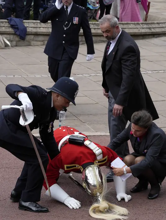 Dengan suhu mencapai 24C, menurut Met Office, seorang prajurit muda harus dibantu berdiri oleh petugas polisi setelah pingsan sebelum upacara dimulai. (Kirsty Wigglesworth / POOL / AFP)