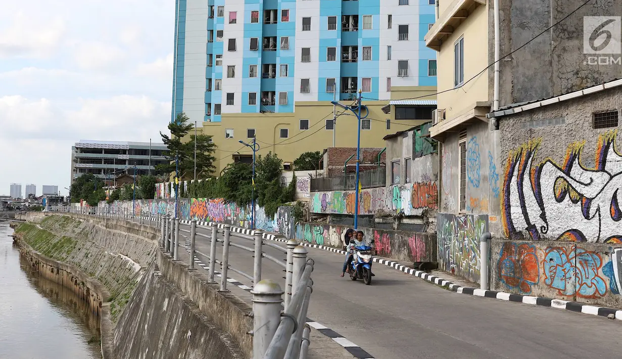 Pengendara melintasi jalur inspeksi Sungai Ciliwung di Jakarta, Kamis (27/12). Mural yang dibuat oleh beberapa komunitas tersebut menjadikan jalur inspeksi Sungai Ciliwung tampak lebih berwarna dan asri. (Liputan6.com/Immanuel Antonius)