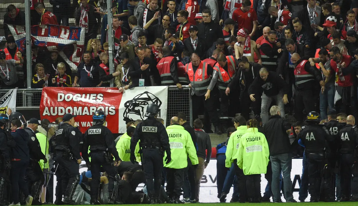 Petugas keamanan membatu suporter yang terjatuh dari tribun saat Amiens melawan Lille LOSC  di Licorne stadium, Amiens, (30/9/2017). Laga tersebut akhirnya ditunda. (AFP/Francois Lo Presti)