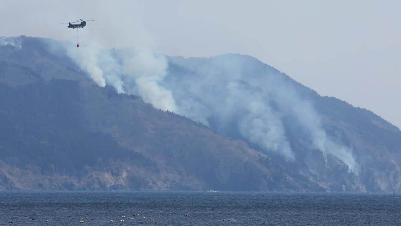 Helikopter terlihat di tengah asap yang mengepul akibat kebakaran hutan di lereng gunung dekat Kota Ofunato, Prefektur Iwate pada 28 Februari 2025. (AFP/Jiji Press)