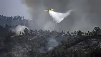 Sebuah pesawat pemadam kebakaran menjatuhkan air di atas api di Odeceixe, selatan Portugal, Selasa (8/8/2023). Ratusan petugas pemadam kebakaran berusaha memadamkan api yang berkobar di Portugal selatan yang telah menghanguskan ribuan hektare lahan dan menyebabkan sekitar 1.400 orang dievakuasi untuk berjaga-jaga. (Patricia DE MELO MOREIRA/AFP)