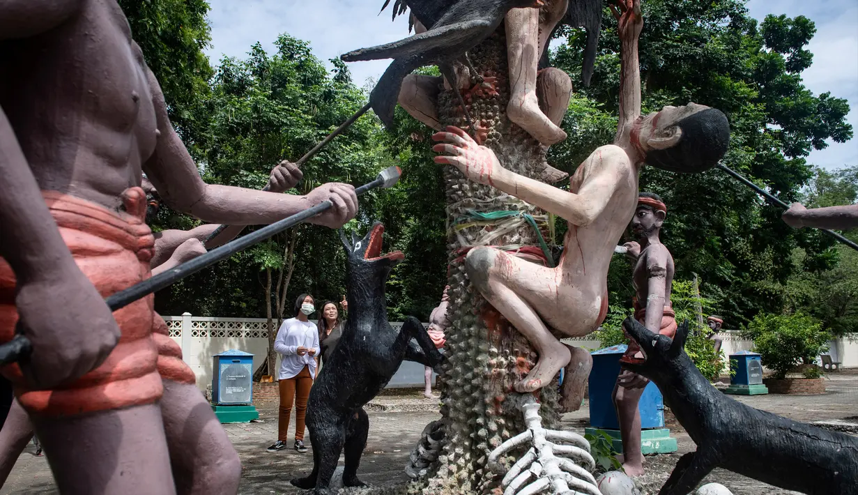 Para pengunjung melihat patung-patung yang menggambarkan nasib orang-orang yang tidak menjunjung tinggi lima ajaran Buddha di sebuah taman yang menggambarkan neraka versi Buddha di kuil Wat Saeng Suk di provinsi pantai Thailand Chonburi (9/7/2020). (AFP/Lillian Suwanrumpha)