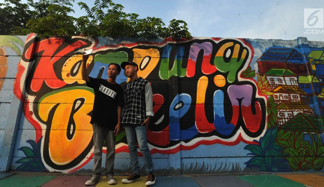 Para remaja berswafoto dengan latar gambar mural/grafiti yang ada di Kampung Bekelir, Jalan Perintis Kemerdekaan, Kota Tangerang, Banten, Selasa (17/4). Jumlah mural/grafiti di kampung ini sekarang mencapai 1.121 gambar. (Merdeka.com/Arie Basuki)