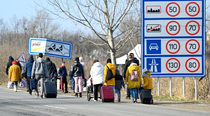 Keluarga Ukraina yang melarikan diri dari konflik di negara mereka sehari setelah Rusia melancarkan serangan militer berjalan dengan barang bawaan mereka setelah melintasi perbatasan Hungaria-Ukraina dekat Beregsurany, Hungaria (25/2/2022). (AFP/Attila Kisbenedek)