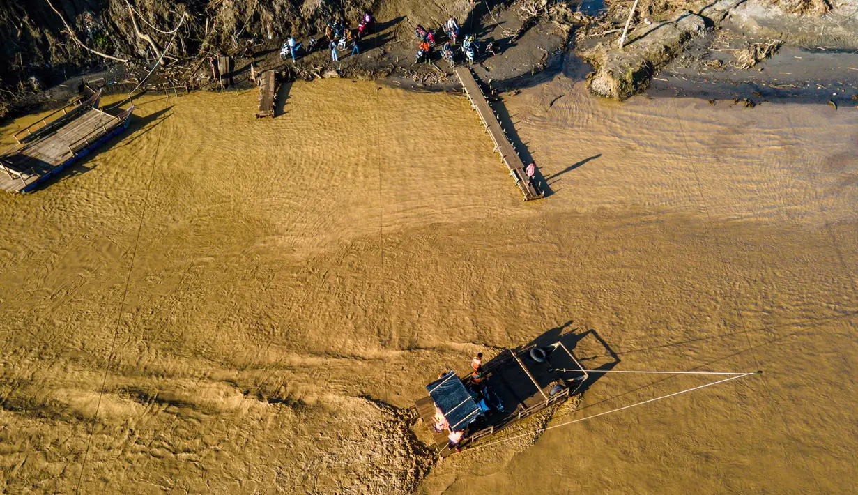 Derasnya air Sungai Peusangan yang menghantam dapat membuat rakit tali berguncang dan rawan kehilangan keseimbangan. Tampak dalam foto, pemandangan udara menunjukkan orang-orang menyeberangi sungai Peusangan menggunakan rakit setelah banjir bandang yang menghancurkan desa-desa di sekitarnya di Kabupaten Bireuen, provinsi Aceh, pada Senin 5 Januari 2026. (CHAIDEER MAHYUDDIN/AFP)