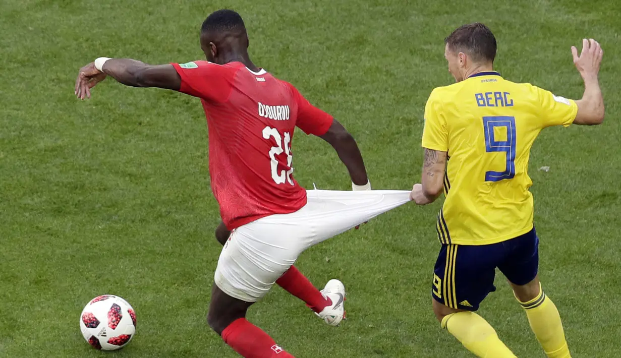 Striker Swedia, Marcus Berg, menarik celana bek Swiss, Johan Djourou, pada babak 16 besar Piala Dunia di Stadion St Petersburg, St Petersburg, Selasa (3/7/2018). Swedia menang 1-0 atas Swiss. (AP/Dmitri Lovetsky)