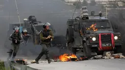 Tentara Israel mengejar pengunjuk rasa saat kendaraan militer mereka terbakar oleh lemparan bom molotov warga Palestina di pinggiran Kota Ramallah, Tepi Barat, Rabu (27/3). Bentrokan ini sebagai bentuk protes terhadap tahanan Palestina yang berada di Israel. (AP Photo/Majdi Mohammed)