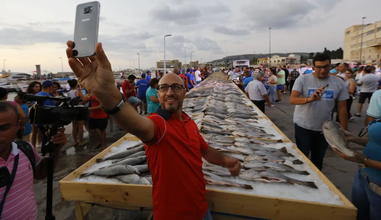 Seorang pria berfoto dengan latar belakang sejumlah ikan yang berhasil memecahkan rekor makanan laut terbanyak di daerah kota pantai Batroun, Minggu (4/9). Menurut panitia, total ikan yang dikumpulnya sebanyak 2 ton 614 kg. (AFP PHOTO/Anwar AMRO)