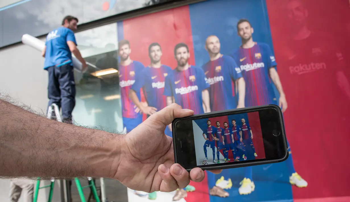 Seorang pria menunjukkan foto di ponselnya yang menampilkan poster pemain depan Barcelona Neymar (kedua kanan) sebelum diganti dengan poster yang terbaru di luar Stadion Camp Nou di Barcelona (2/8). (AFP Photo/Josep Lago)