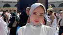 Yuni Shara saat berpose di depan Kakbah. Dia mengenakan gamis putih yang dipadukan dengan hijab bercorak. (Foto: Instagram/ yunishara36)