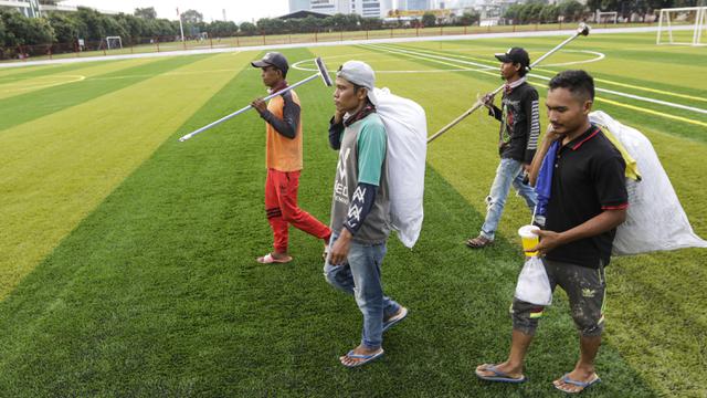 Para pekerja berjalan usai menyelesaikan pekerjaan di Lapangan Aldiron. (Bola.com/M. Iqbal Ichsan)