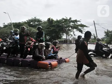 Pengendara sepeda motor menggunakan jasa rakit saat banjir melanda Cempaka Putih, Jakarta, Minggu (23/2/2020). Pengendara memanfaatkan jasa angkutan rakit yang ditawarkan warga agar dapat melewati banjir. (merdeka.com/Iqbal S. Nugroho)