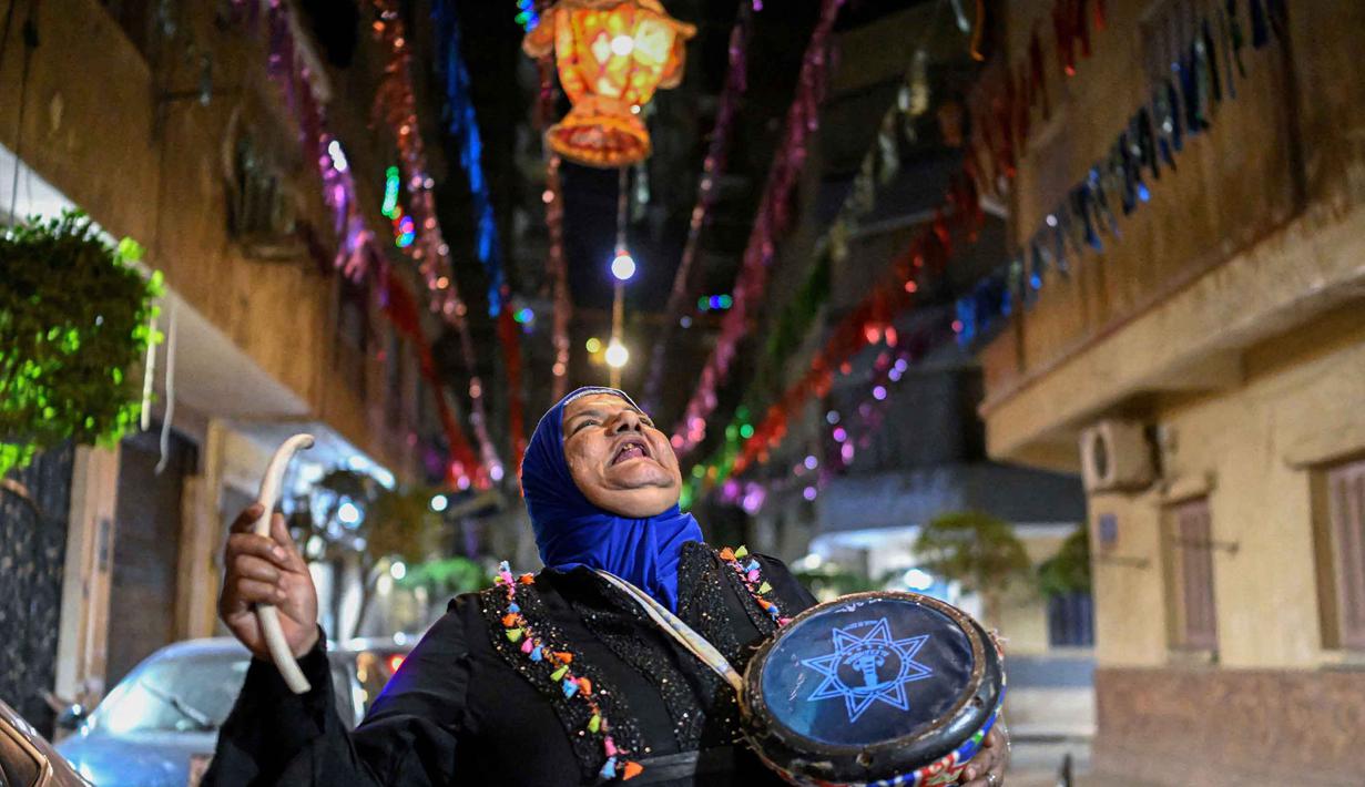 Dalal, seorang wanita Mesir yang dikenal sebagai 'musaharati', berjalan di sepanjang jalan sambil memukul gendang dan menyerukan umat Muslim untuk bangun dan makan sahur selama bulan suci Ramadan di distrik Hadayek el-Maadi, selatan Kairo pada Minggu 1 Maret 2026. Musaharati merupakan tradisi kuno Ramadan di negara-negara Arab, Palestina, Mesir, dan lainnya. (Khaled DESOUKI/AFP)