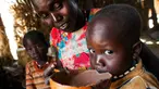 Seorang wanita bernama Nybol Madut memberi minum semangkuk alkohol lokal kepada anaknya di tempat penampungan di Sudan Selatan (22/11). (AFP Photo/Albert Gonzalez Farran)