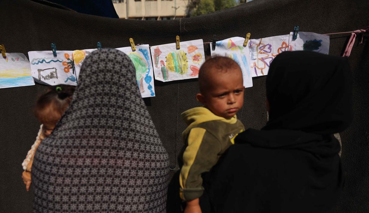 Dalam coretannya, mereka mengungkap penderitaan, kengerian, dan harapan mereka akan terjadinya perdamaian. Tampak dalam foto, orang-orang yang membawa anak-anak melihat pameran di sebuah sekolah yang diubah menjadi tempat penampungan bagi pengungsi Palestina di kawasan Al-Rimal, Kota Gaza, pada 5 November 2025. (Omar AL-QATTAA/AFP)