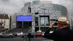 Seorang pria mengambil gambar potret para petugas kesehatan yang ditempelkan di bagian depan Bastille Opera di Paris, Prancis, Jumat (10/7/2020). Potret hitam putih itu untuk memberi penghormatan kepada pekerja medis yang berjuang menghadapi Corona Covid-19. (AP Photo/Francois Mori)