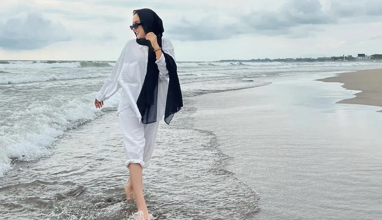 Berada di pantai, ia mengenakan pashmina dipadukan atasa oversize kemeja dan celana putih.(@cita_citata)