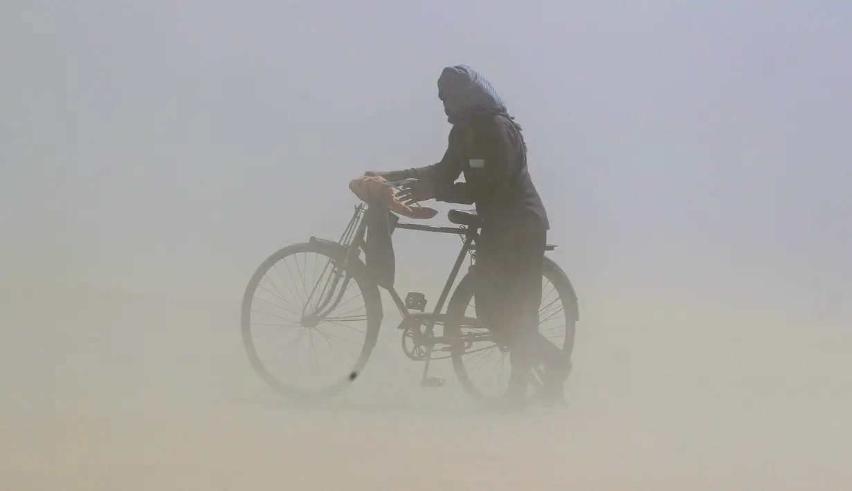 Seorang pria menutupi wajahnya saat ia mendorong sepeda melalui badai pasir di tepi sungai Gangga di Allahabad, India, Selasa (12/4/2016).  (REUTERS/Jitendra Prakash)