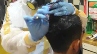 Seorang tukang cukur mengenakan alat pelindung diri (APD) saat memangkas rambut pelanggannya di Chemot Barbershop, Ciawi, Bogor, Jawa Barat, Minggu (5/4/2020). Penggunaan APD tersebut sebagai antisipasi agar lebih waspada terhadap penularan virus corona Covid-19. (merdeka.com/Arie Basuki)
