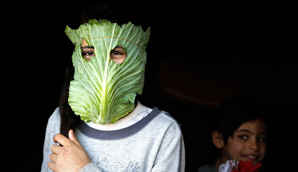 Seorang anak berpose dengan masker dari kubis di tengah wabah pandemi corona (Covid-19) di Beit Lahia di Jalur Gaza utara (16/4/2020). Di tengah pandemi Covid-19, seorang ibu di Jalur Gaza utara mencoba menghibur anak-anaknya dengan masker yang dibuat dari sayuran kubis. (AFP/Mohamed Abed)