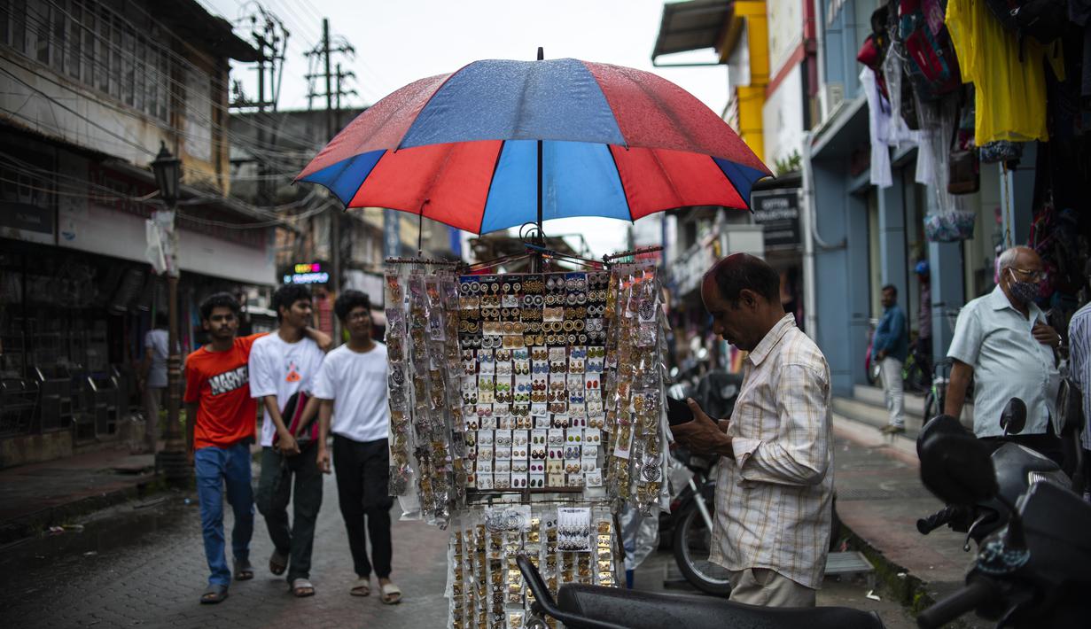 Seorang pedagang kaki lima menggunakan payung untuk melindungi anting-antingnya dari hujan di Kochi, negara bagian Kerala, India, Rabu (6/7/2022). Negara bagian selatan itu telah mewajibkan penggunaan masker di tempat-tempat umum menyusul meningkatnya kasus COVID-19. (AP Photo/ RS Iyer)