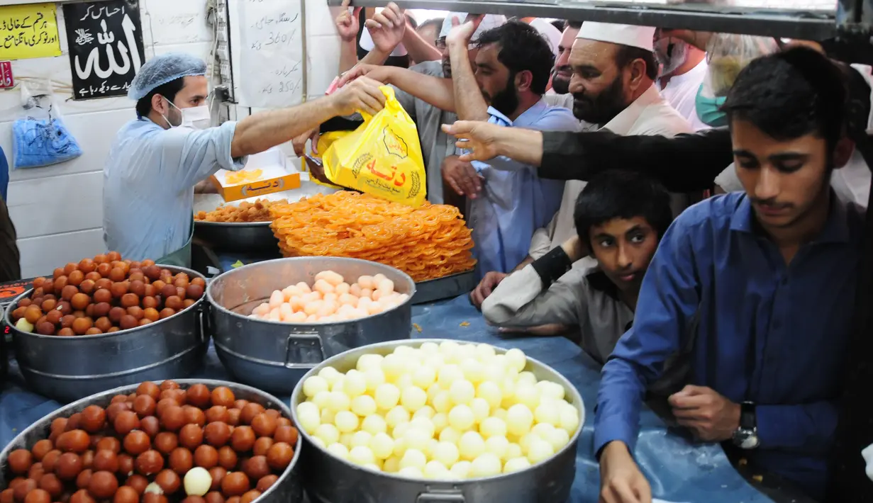 Orang-orang membeli penganan manis tradisional di hari raya Idul Fitri di Peshawar, Pakistan barat laut, pada 25 Mei 2020. Warga Pakistan memiliki tradisi memakan penganan manis saat merayakan Idul Fitri, yang menandai akhir bulan puasa Ramadan. (Xinhua/Saeed Ahmad)