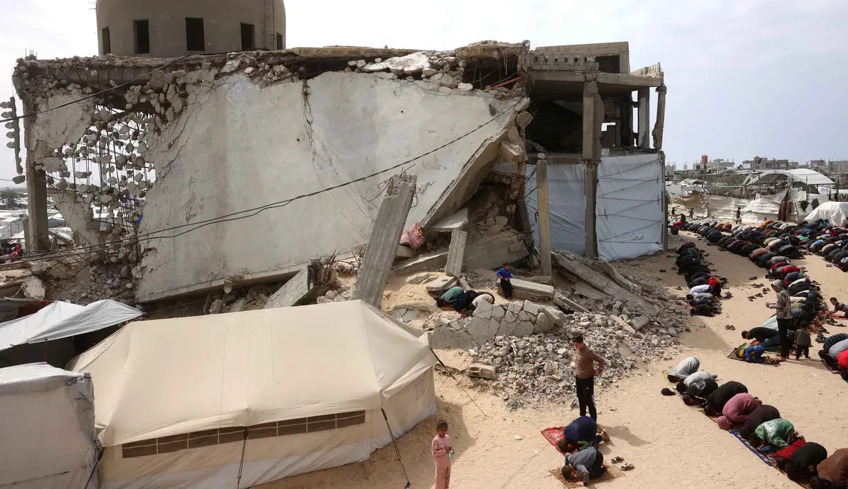 Meski harus berhadapan dengan ancaman bahaya dan reruntuhan bangunan, warga di Gaza tetap memadati lokasi salat Jumat pada 13 Maret 2026. Tampak dalam foto, umat Muslim Palestina berdoa saat salat Jumat terakhir di bulan suci Ramadan 1447 Hijriah, di luar Masjid Al-Talbani, yang dihancurkan oleh militer Israel di Khan Yunis, Jalur Gaza selatan pada Jumat 13 Maret 2026. (Bashar Taleb/AFP)