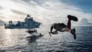 Menggunakan kapal selam Neptune milik organisasi nirlaba OceanX di perairan lepas pantai Pulau Sulawesi. Tampak dalam foto yang diambil pada 9 Januari 2026, menunjukkan awak kapal OceanXplorer, sebuah kapal penelitian yang dioperasikan oleh organisasi nirlaba kelautan OceanX, melompat ke laut dari sebuah perahu untuk berenang menuju kapal selam yang muncul ke permukaan dan memasang tali penyelamat di perairan lepas pantai Pulau Sulawesi. (YASUYOSHI CHIBA/AFP)
