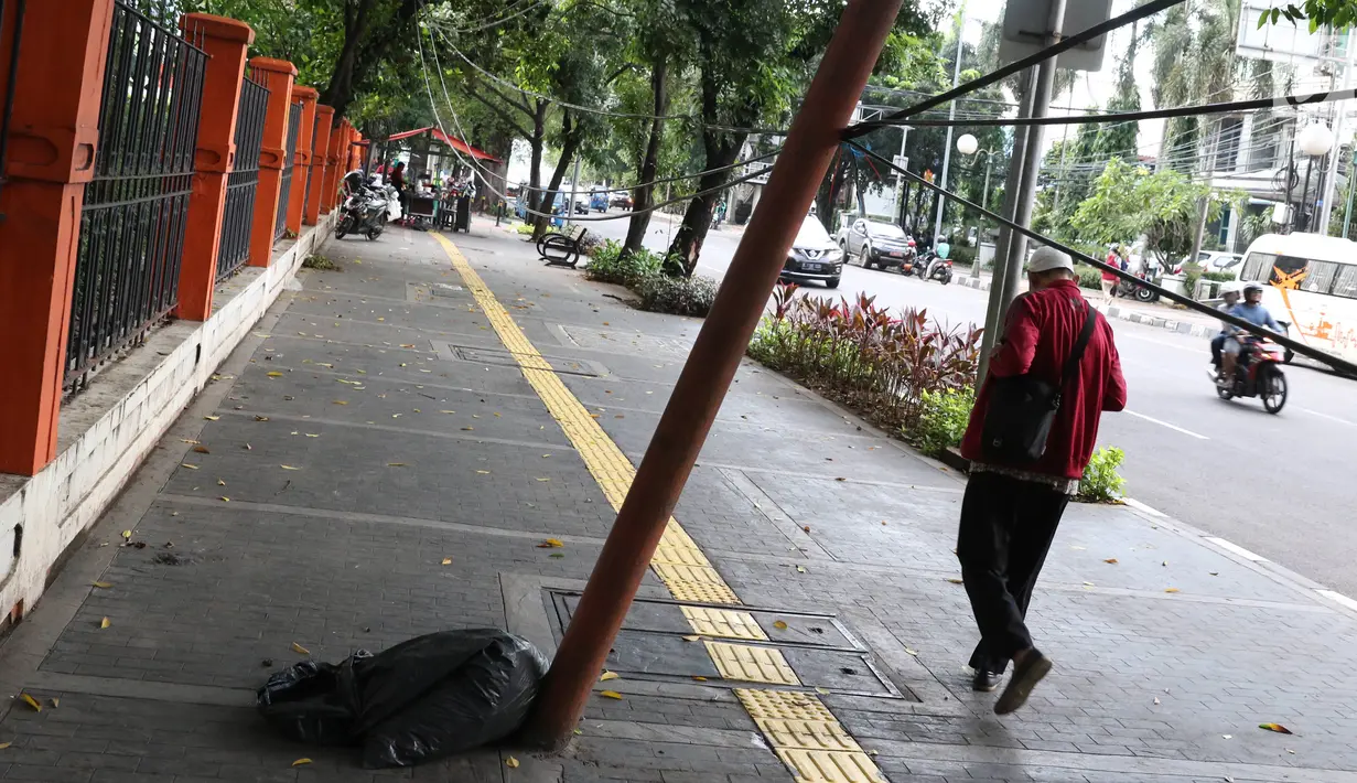 Pejalan kaki melintas di dekat tiang yang miring di Jalan Gedung Kesenian, Jakarta, Jumat (22/2). Keberadaan tiang miring tersebut membahayakan keselamatan pejalan kaki karena kabel yang turut menjuntai hingga ke bawah. (Liputan6.com/Immanuel Antonius)